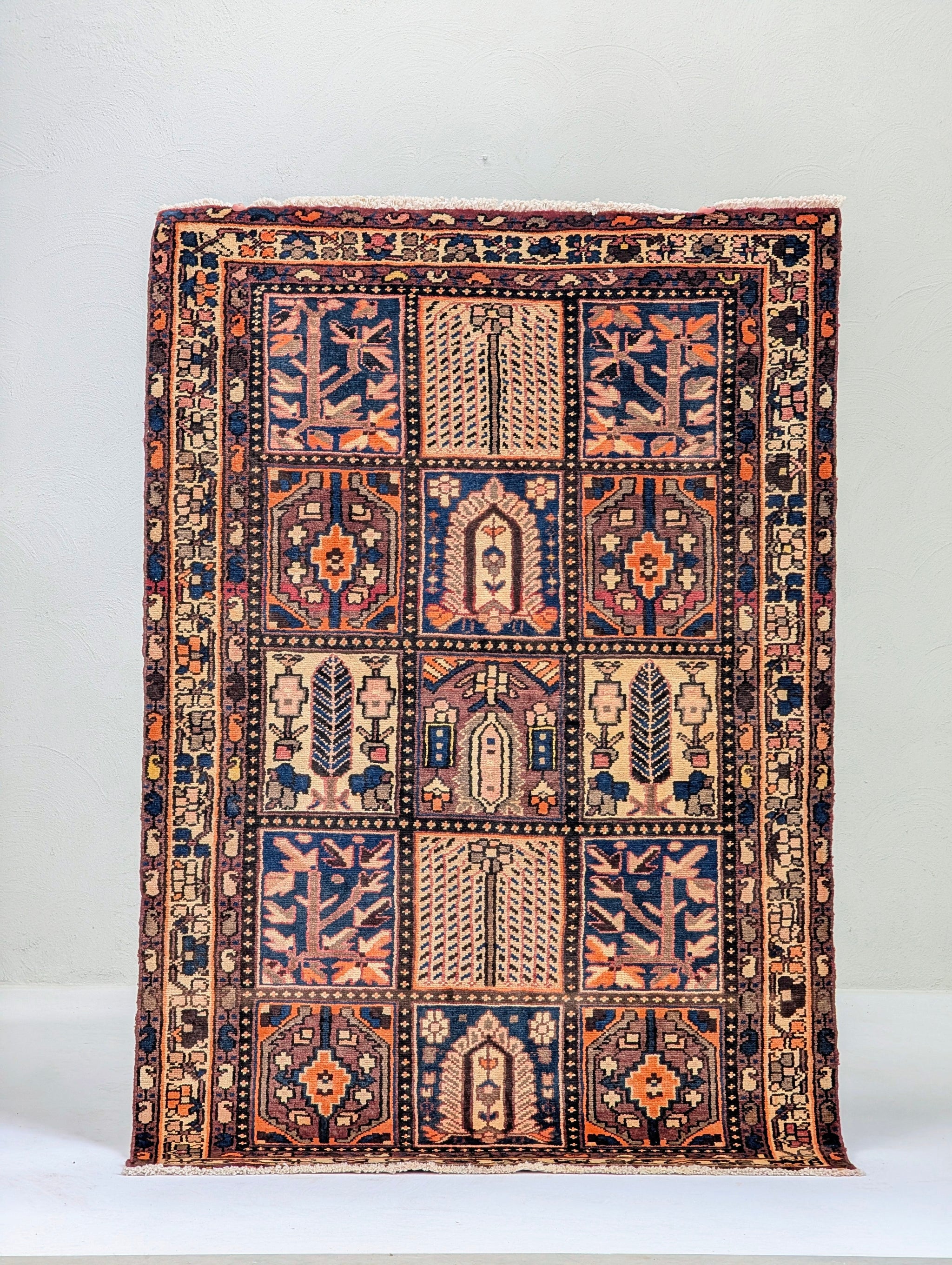 Tan accent rug with dragon motifs in the center and corners, held against a white wall.