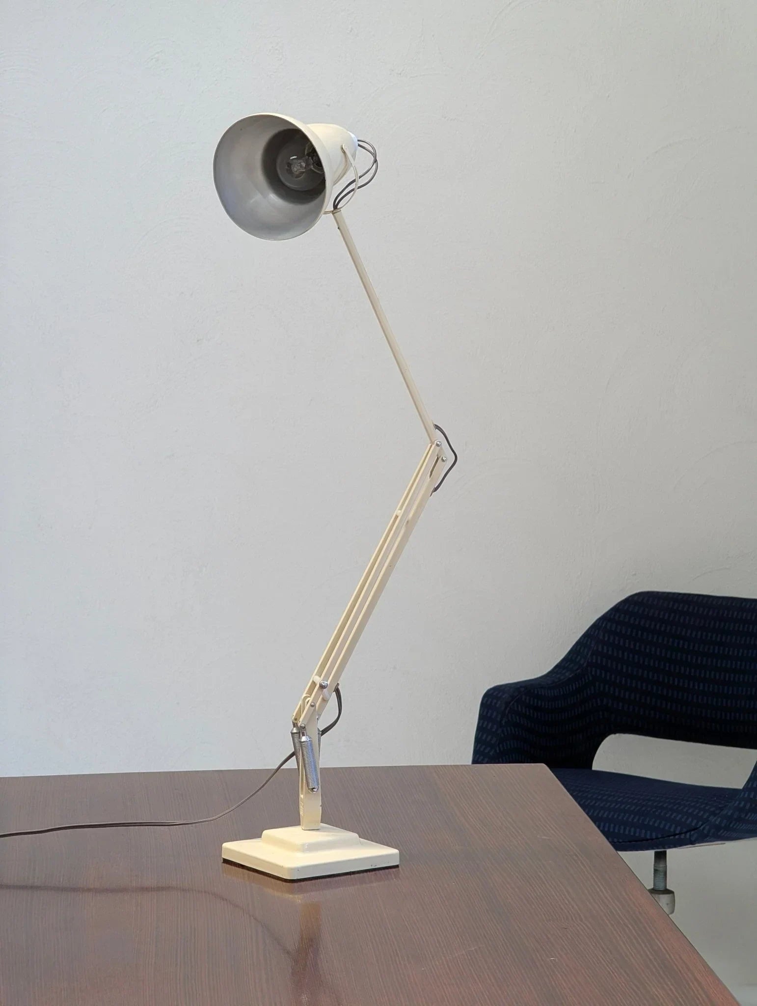 Vintage white Anglepoise desk lamp on wooden desk beside blue chair against white wall