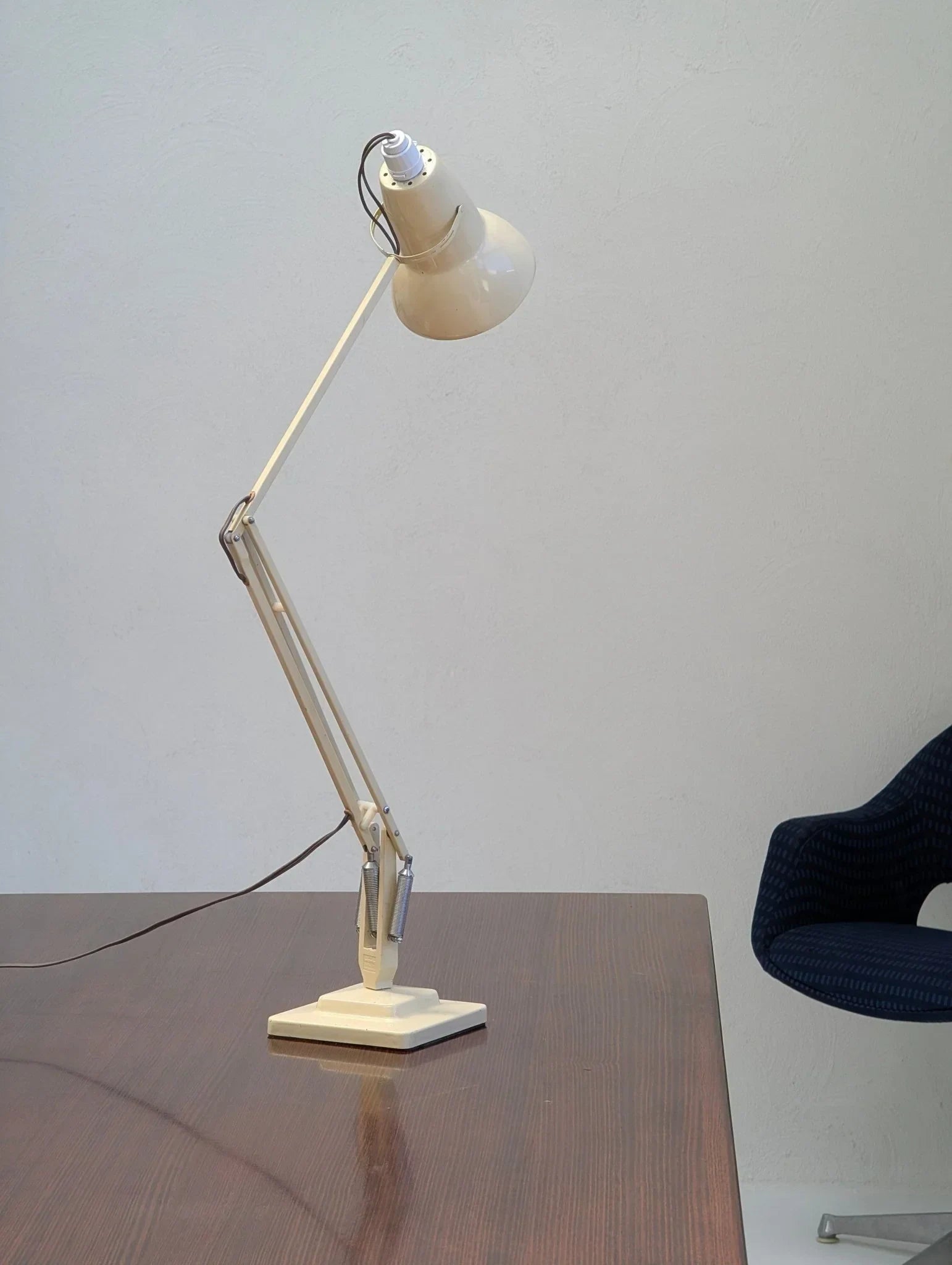 Vintage cream Herbert Terry Anglepoise desk lamp on wooden table beside dark blue chair