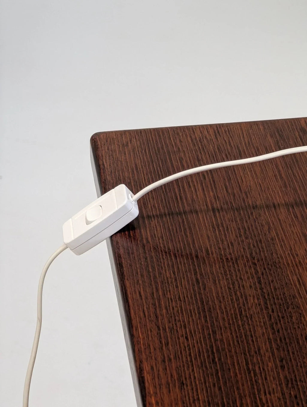 White inline switch on cable resting on dark wood desk corner, minimalist setting