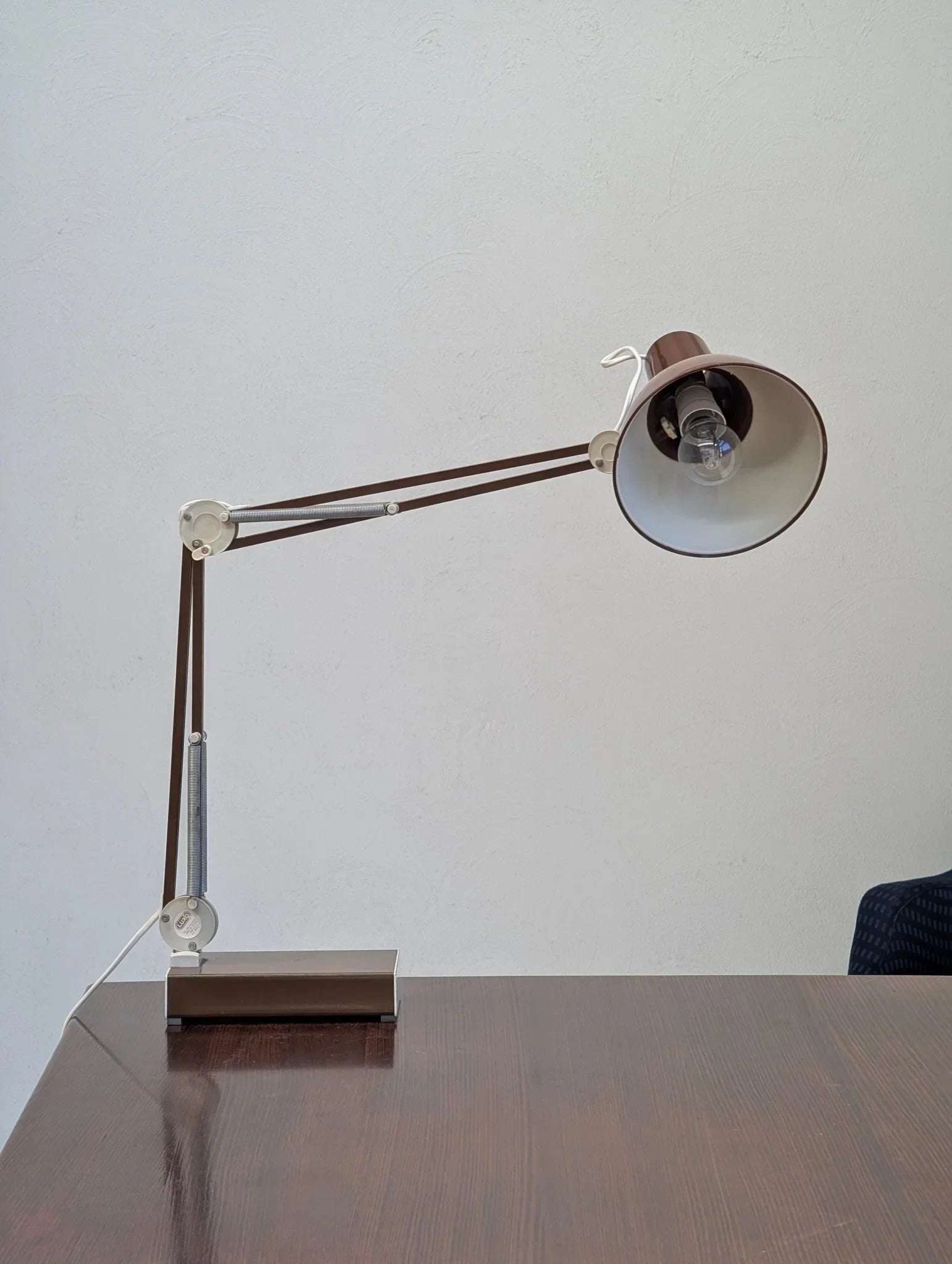 1970s brown adjustable architect task lamp on wood desk with white wall background