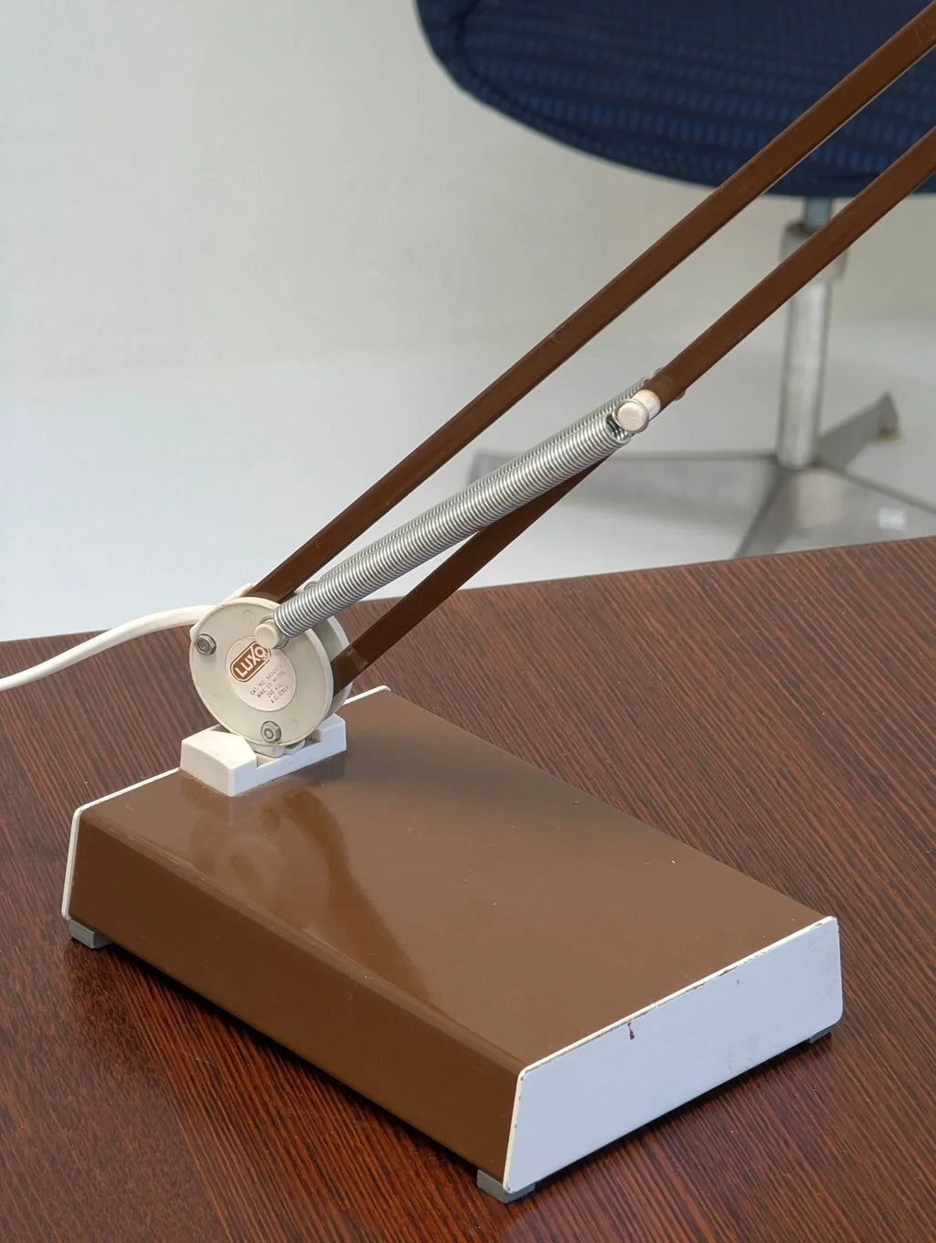 1970s brown architect task lamp base on wood desk, visible spring arm, blue chair background