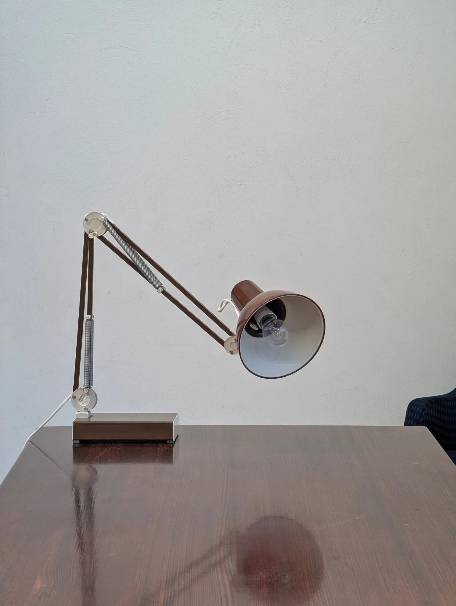 1970s brown Luxo L-1 architects task lamp on wooden desk against plain wall