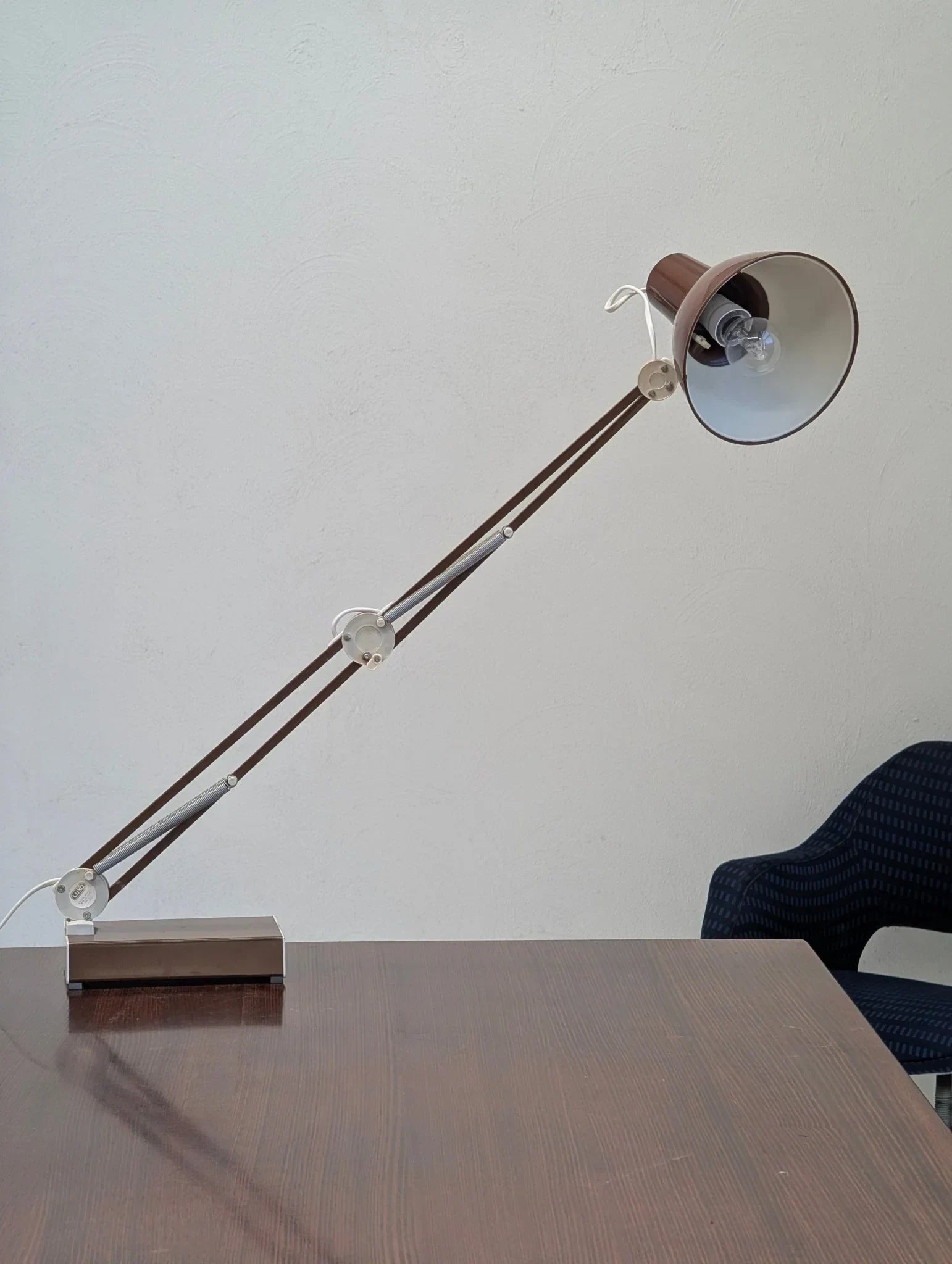 1970s brown L-1 architect task lamp on wood desk near blue chair, white wall background