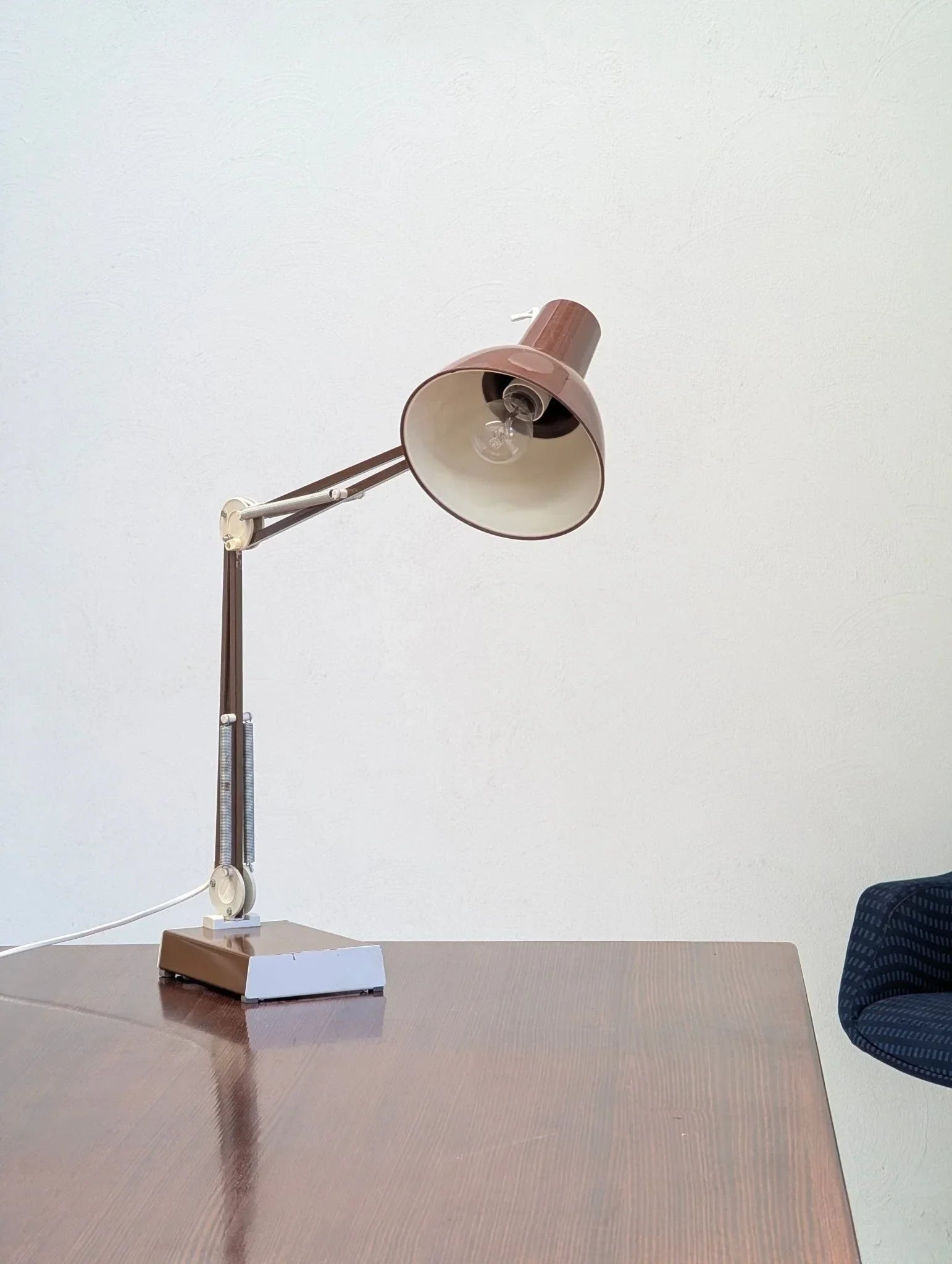 1970s brown Luxo L-1 architects task lamp on wooden desk against white wall