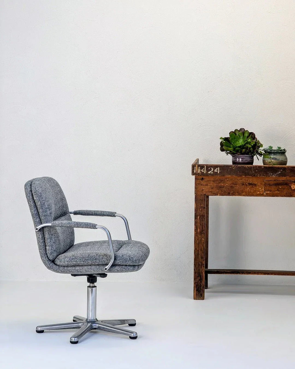 80s executive swivel armchair in textured wool beside rustic wooden desk with succulents