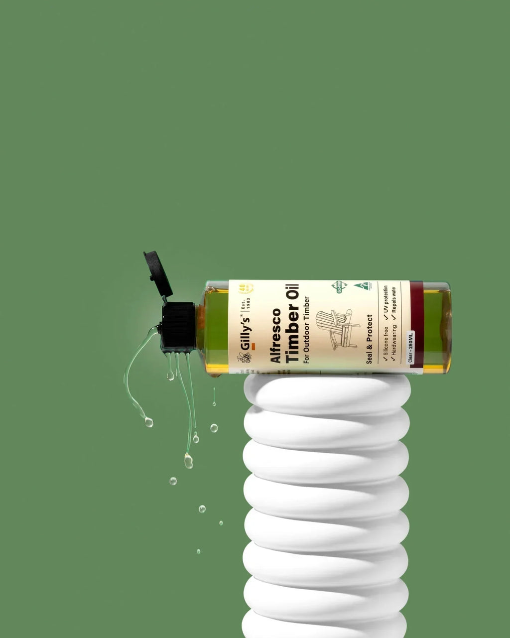 Gilly’s Alfresco Timber Oil 250ml bottle dripping liquid on a sculpted white pedestal, green background