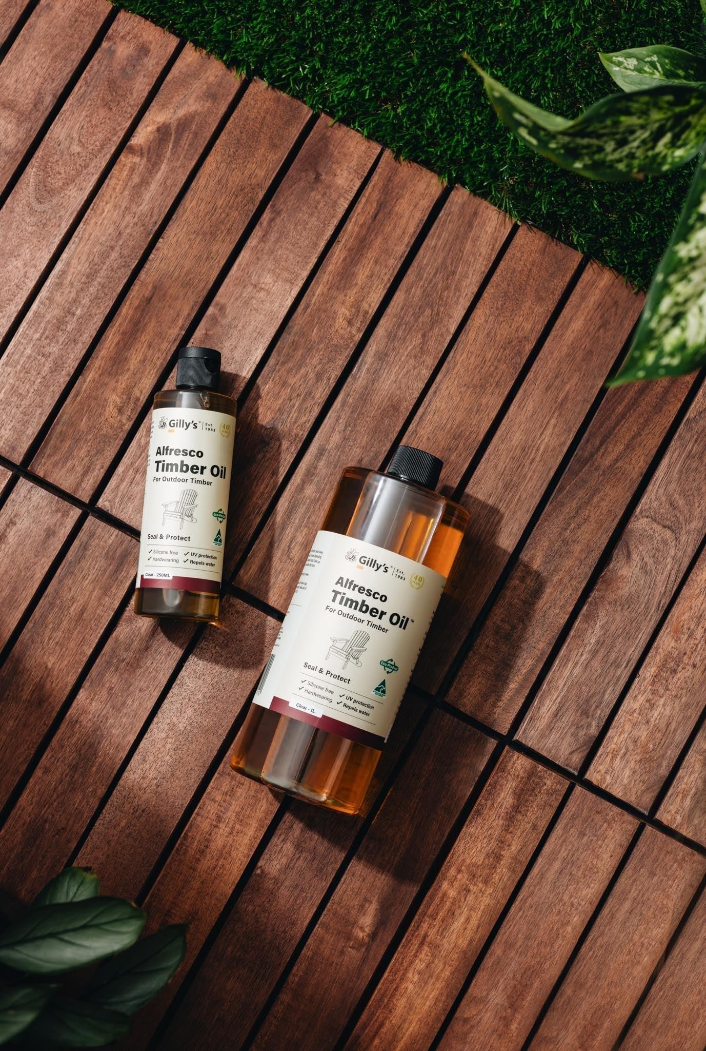 Gilly's Alfresco Timber Oil bottles on outdoor wooden decking with green plants