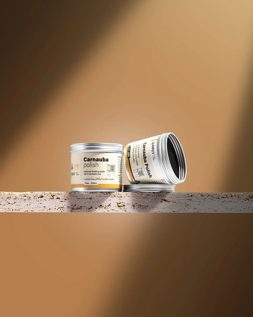 Two Gilly's Carnauba Polish 200ml tins on a textured stone shelf with a brown background.