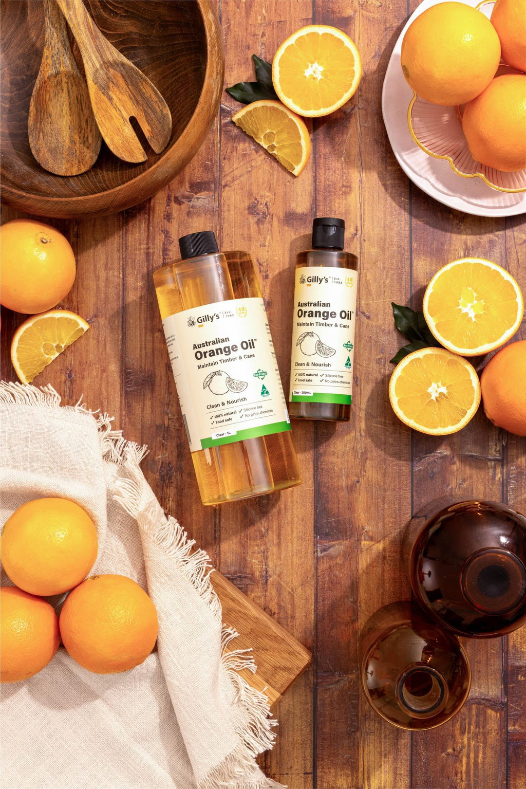 Gilly's Australian Orange Oil bottles with fresh oranges, wooden bowl, and rustic wood table