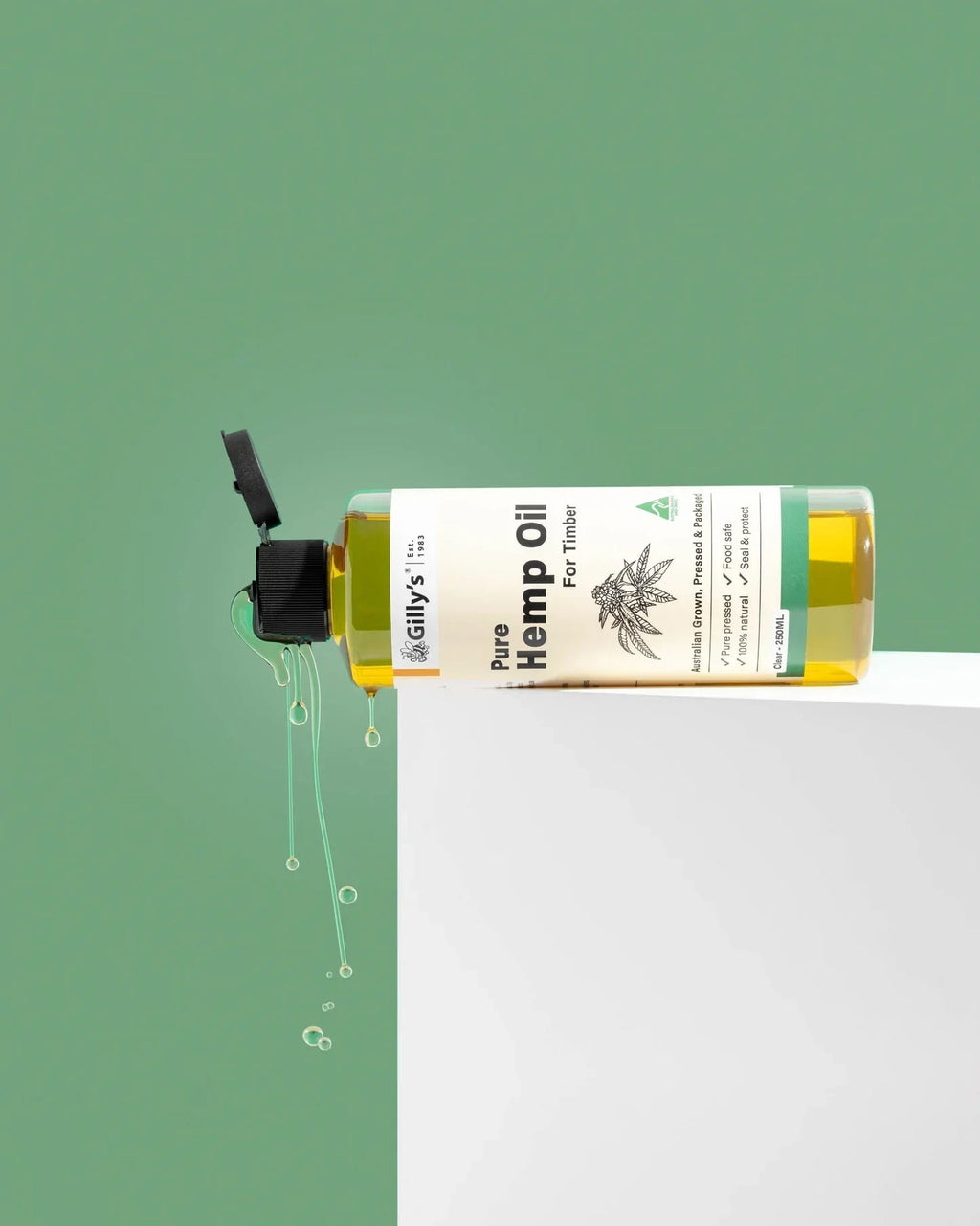 Gilly's Pure Hemp Oil for timber bottle dripping oil over white surface with green background