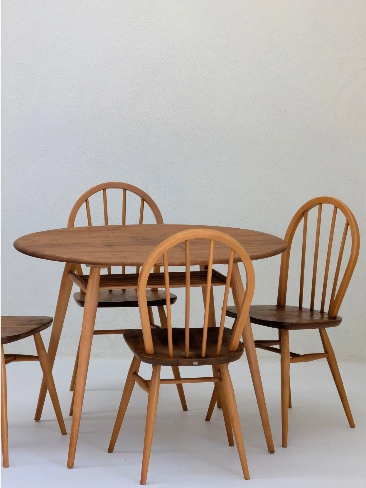 Round wooden dining table set with four spindle-back chairs on a white background