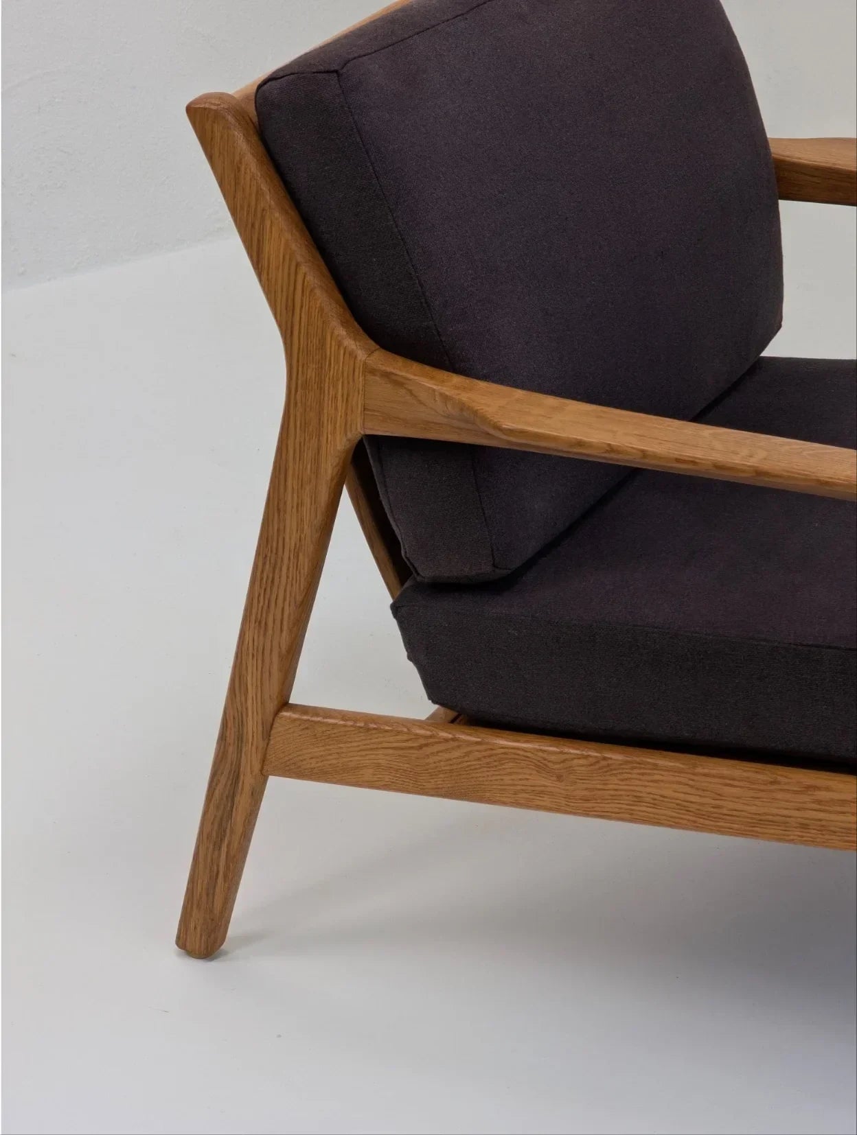 Mid-century modern chair with wooden frame and dark grey cushions on a white floor