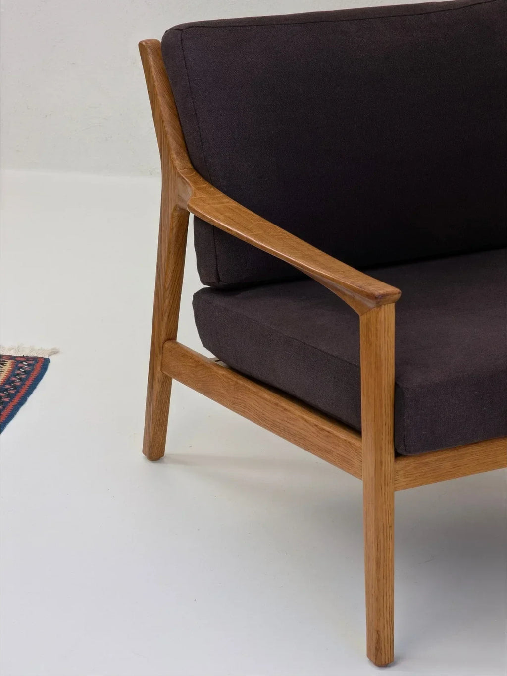 Mid-century modern wooden armchair with dark gray cushions on white floor