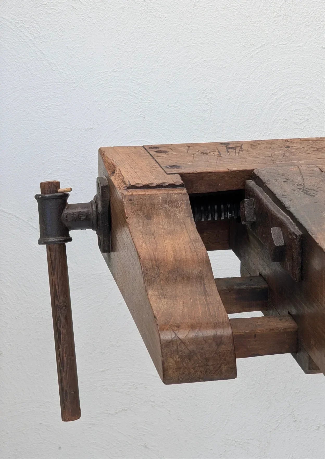 Close-up of vintage wooden workbench vise with iron handle against white wall