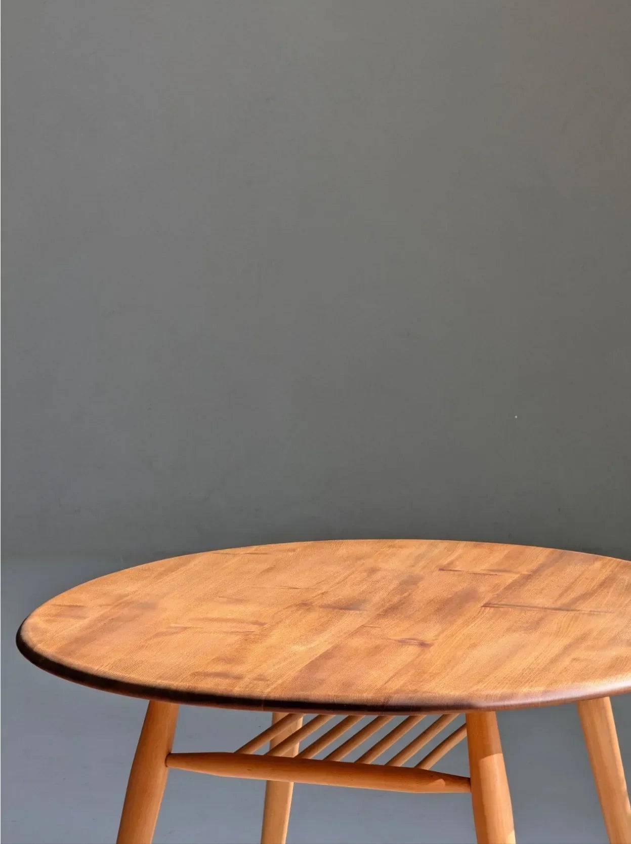 Round wooden table with light wood finish against a plain gray wall.