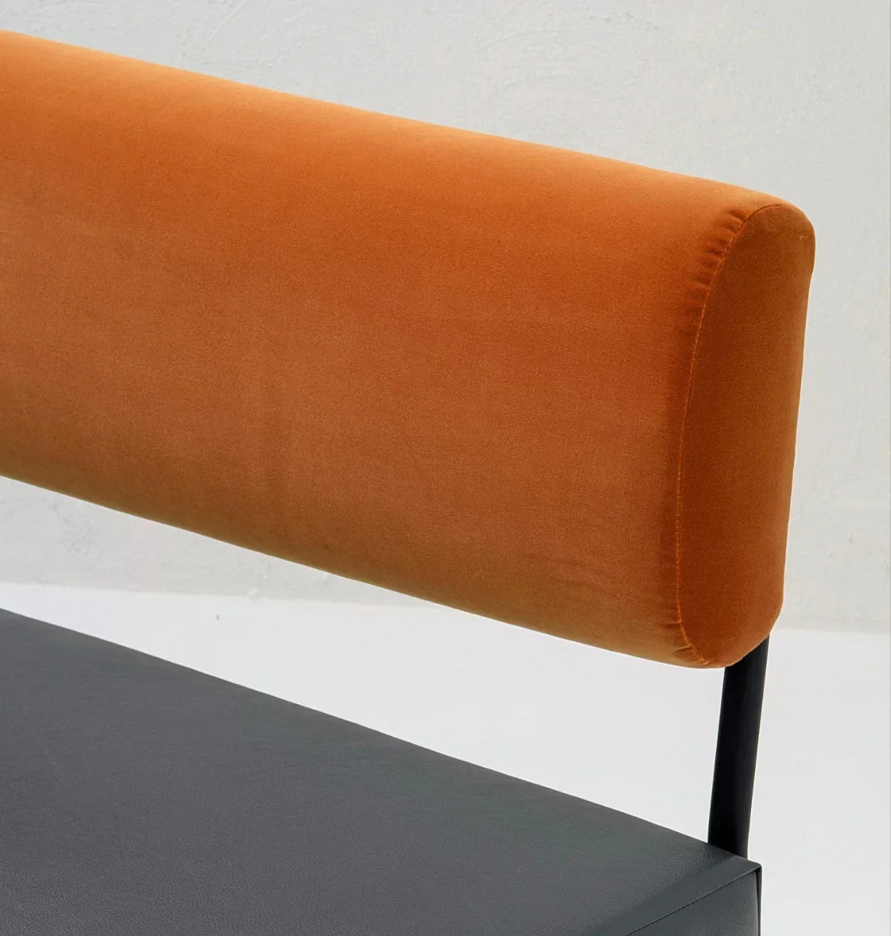 Modern chair with orange velvet cylindrical backrest and black leather seat