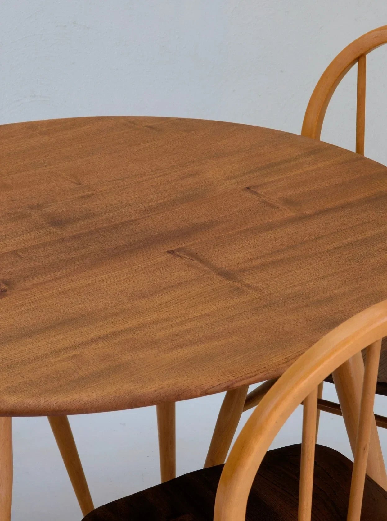 Round wooden dining table with light wood chairs against a plain background