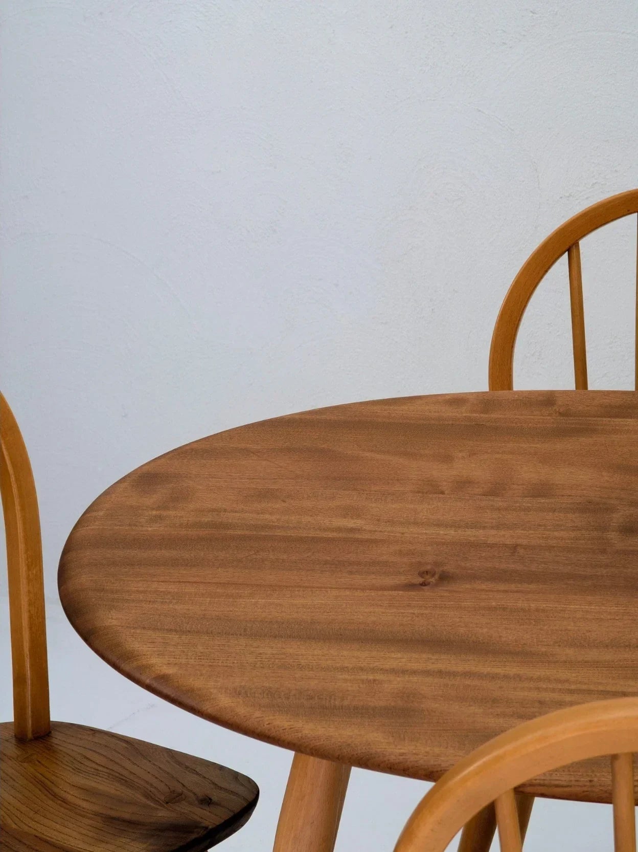 Minimalist round wooden dining table with two matching chairs against a plain white wall
