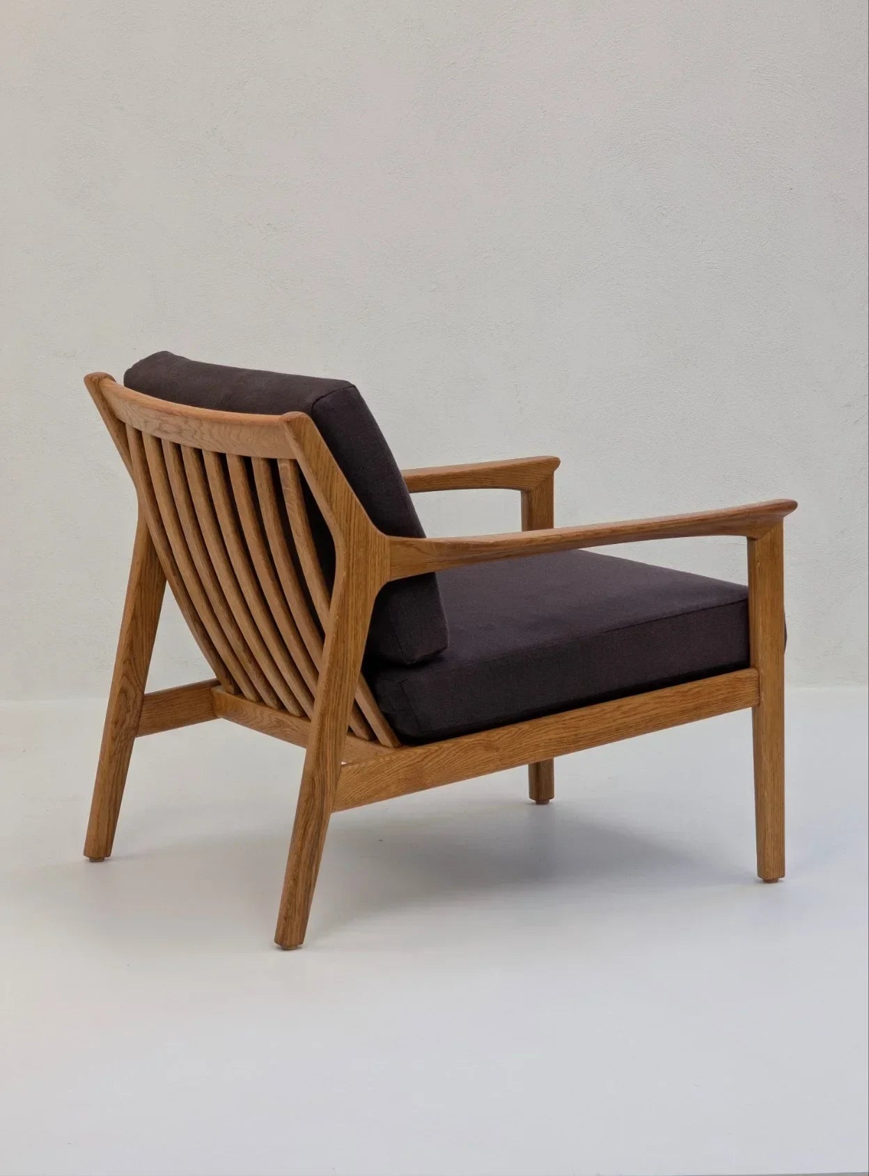 Mid-century modern wooden lounge chair with dark cushions against a light wall