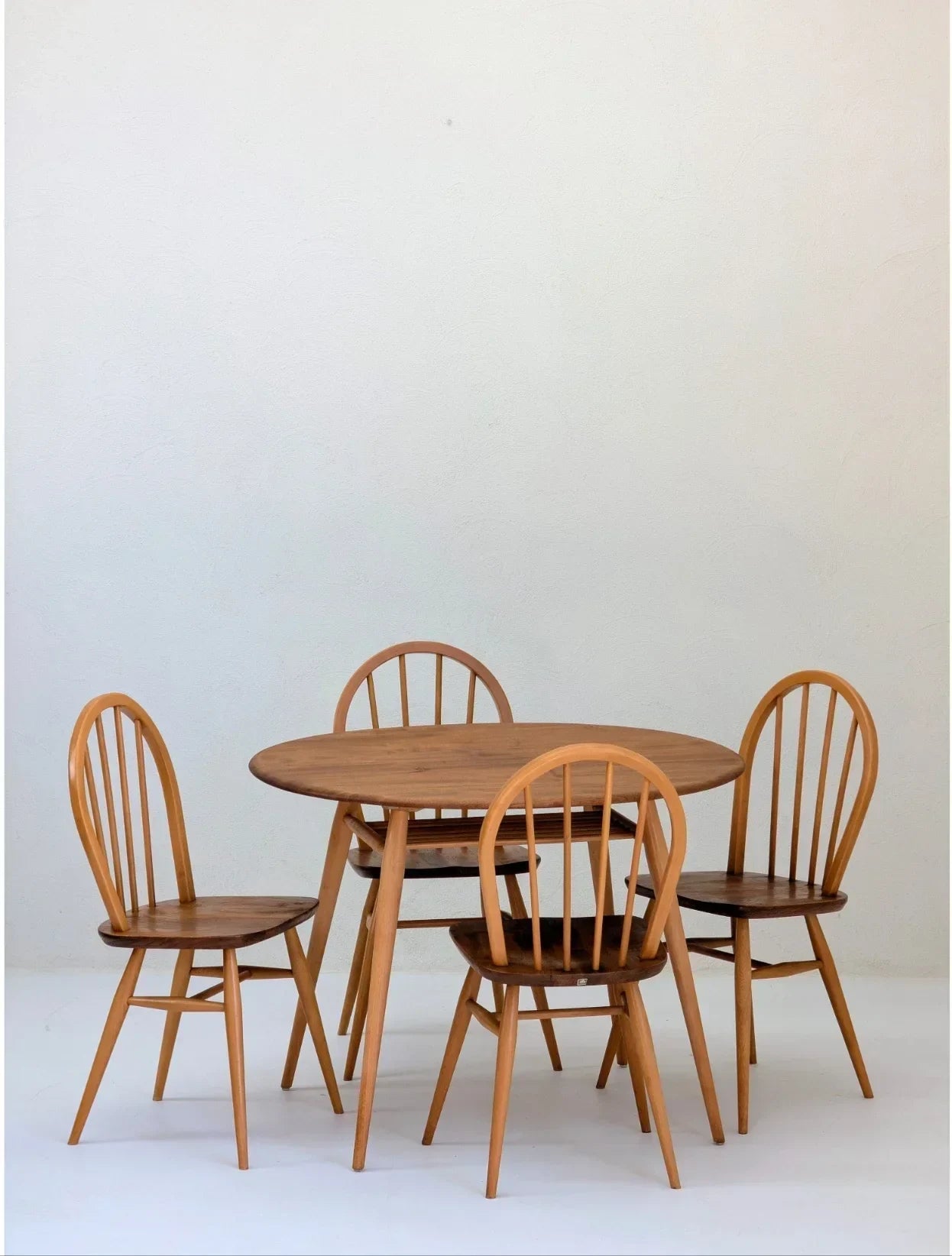 Mid-century modern wooden dining table with four spindle back chairs on a white background