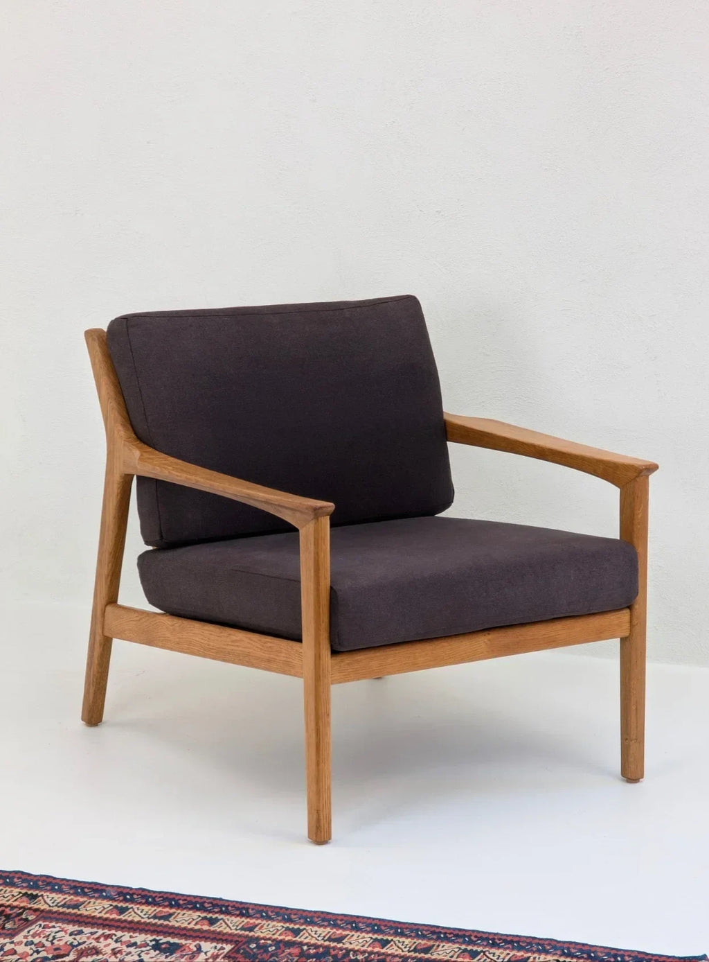 Modern armchair with dark cushions and wooden frame on white floor next to patterned rug