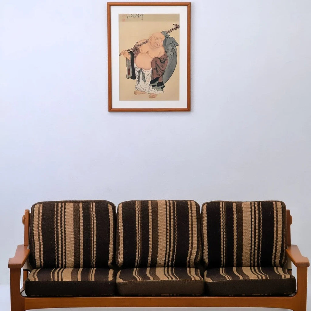 Striped brown and beige cushioned wooden sofa under framed traditional Asian artwork on white wall