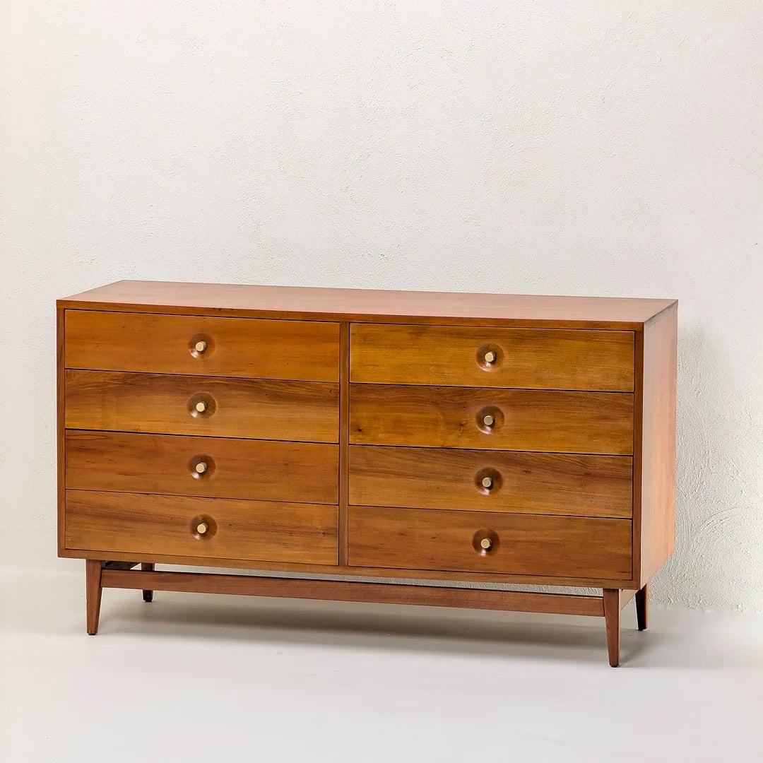 Mid-century modern wooden dresser with eight drawers and round brass knobs against white wall