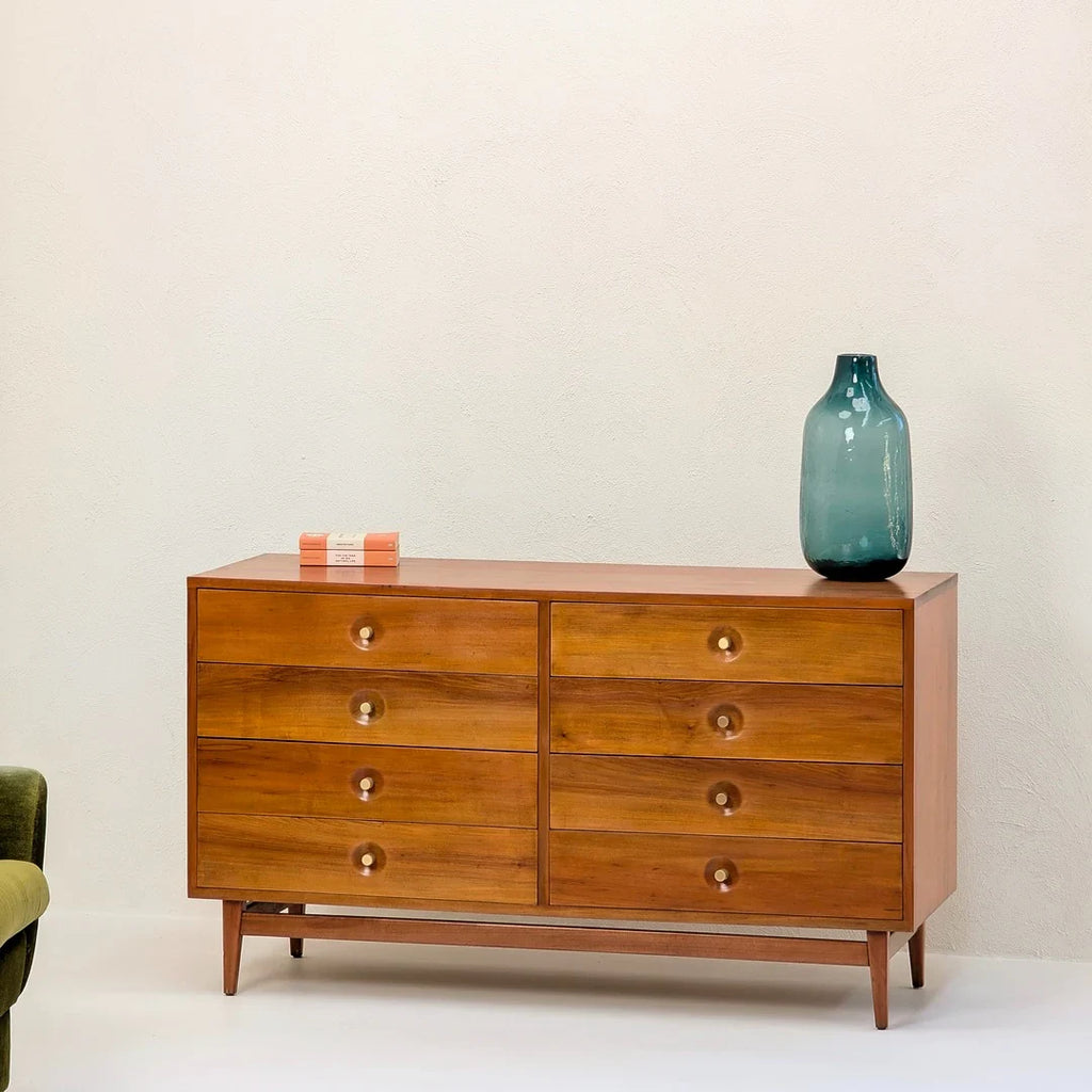 Mid-century modern wooden dresser with eight drawers, blue glass vase, and orange book on top