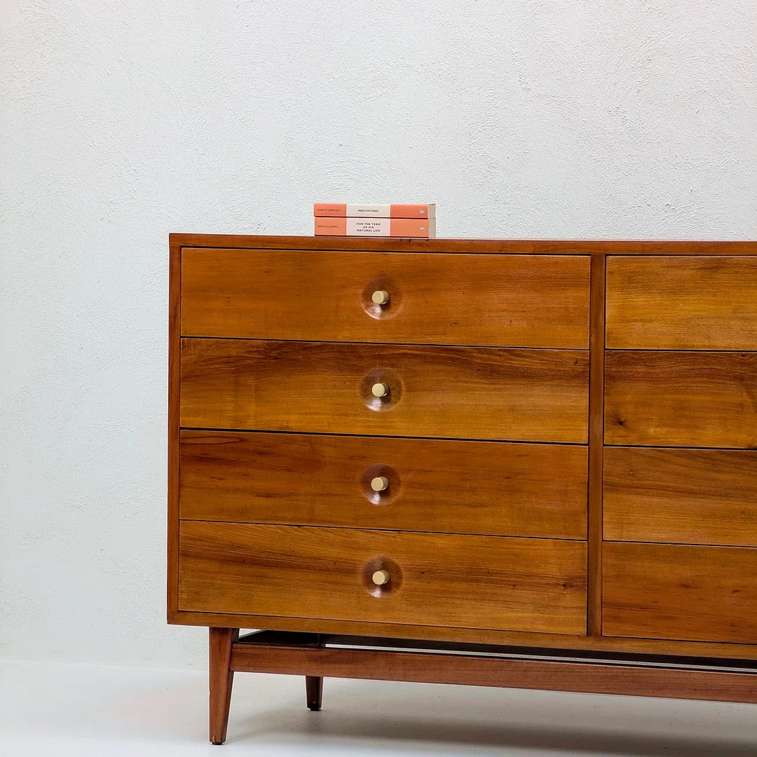 Mid-century modern wooden dresser with brass knobs and two stacked books on top against white wall