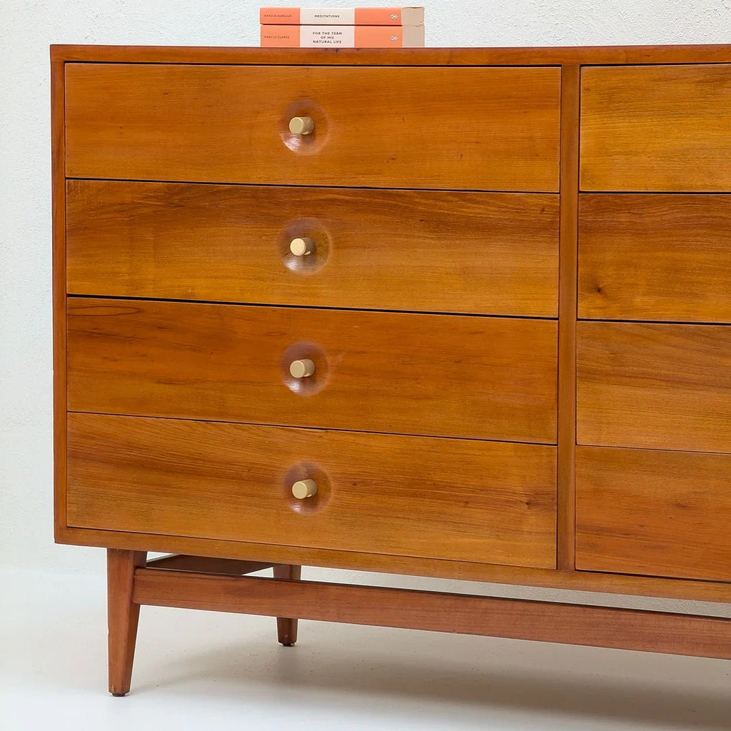 Mid-century modern wooden dresser with four brass knobs and two books on top against white wall