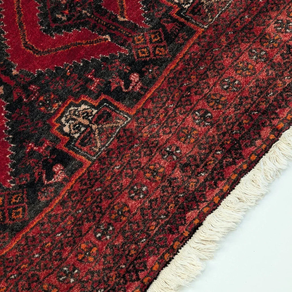 Close-up of a red Persian rug with intricate geometric patterns and white fringe