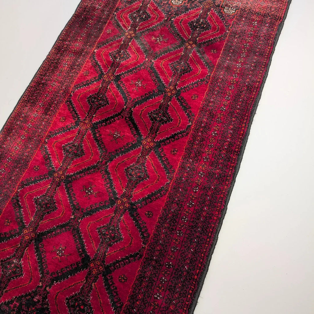 Red Persian runner rug with geometric diamond patterns and intricate borders on a white floor