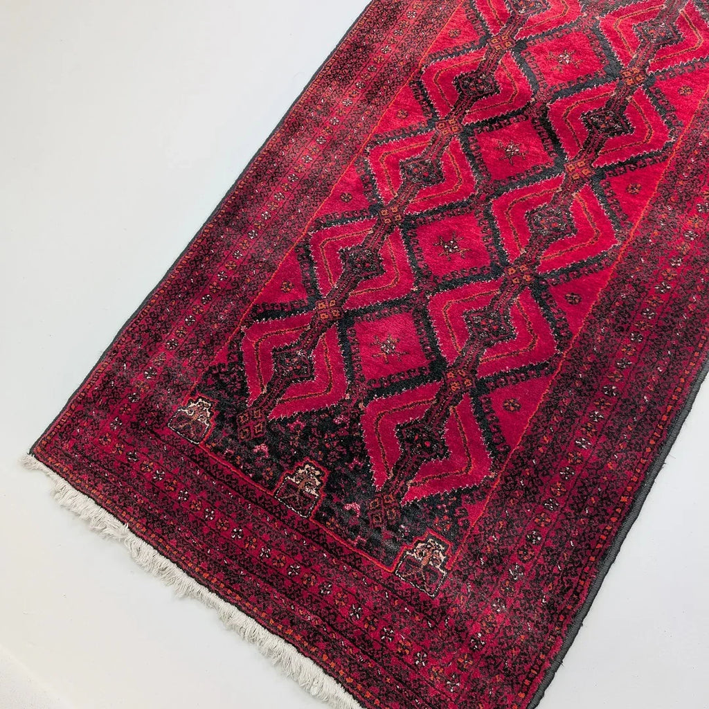 Red Persian runner rug with geometric diamond pattern and decorative fringe on white floor