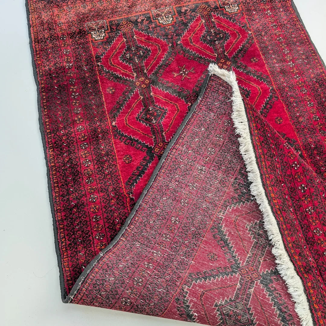 Red Persian rug with geometric patterns and visible fringed corner on a light background