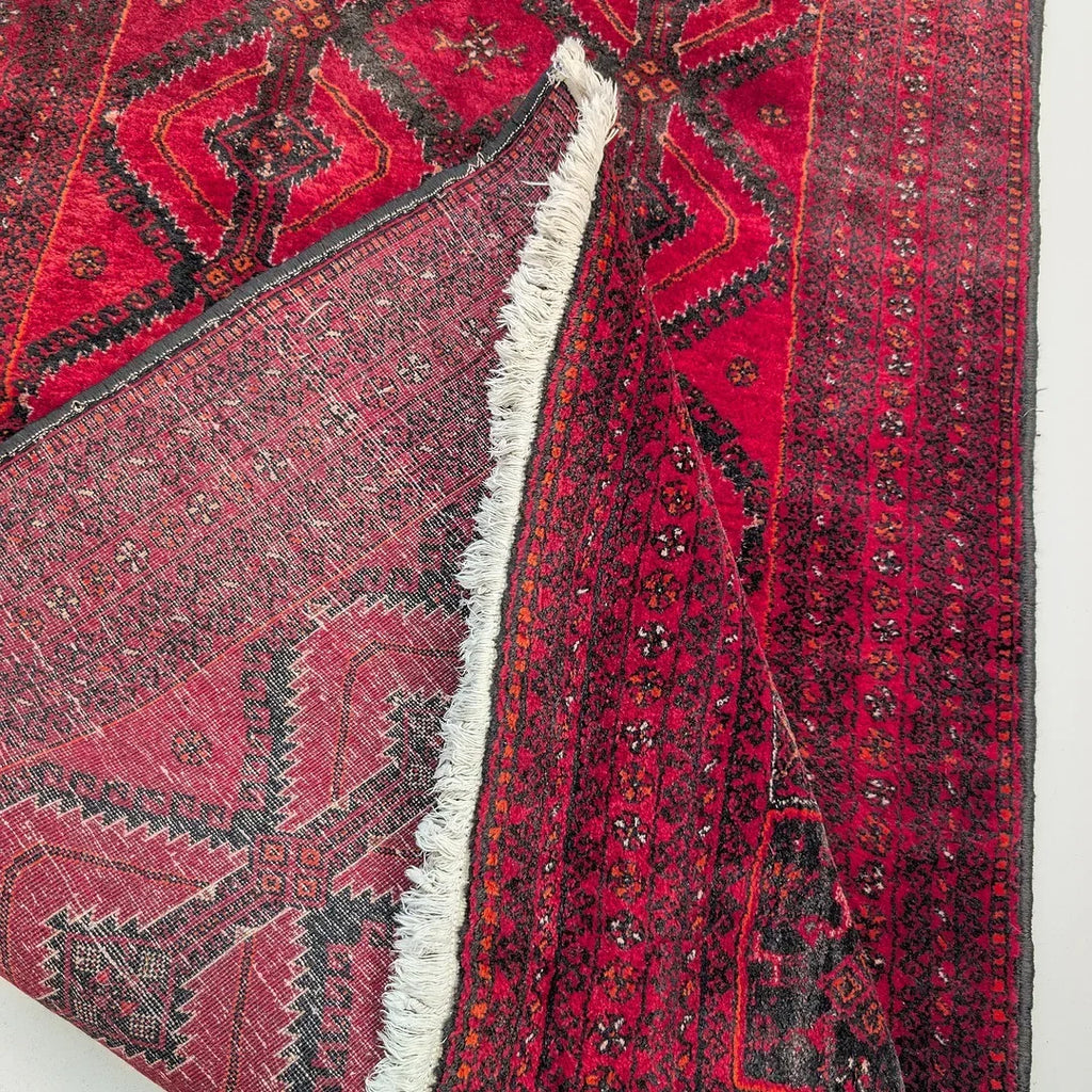Red Persian rug with geometric black patterns and a folded corner showing the backside