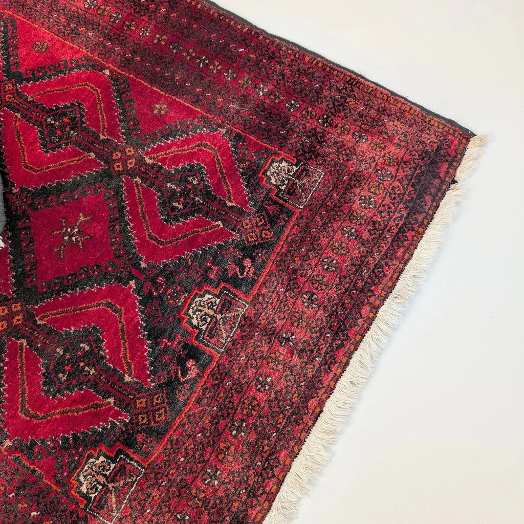 Corner of a vintage red Persian rug with geometric patterns and fringe on a white background