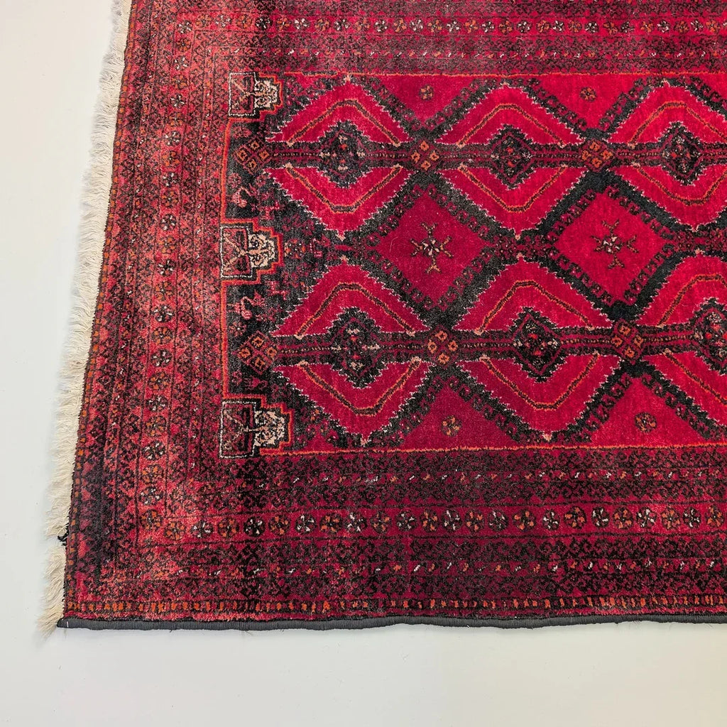 Red vintage Persian rug with geometric diamond pattern and intricate border on white floor