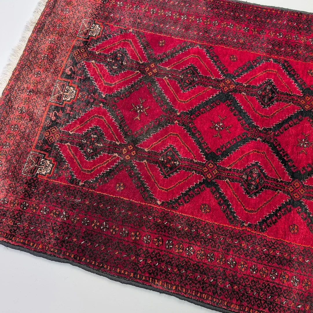 Red Persian rug with geometric black and orange patterns and detailed border design