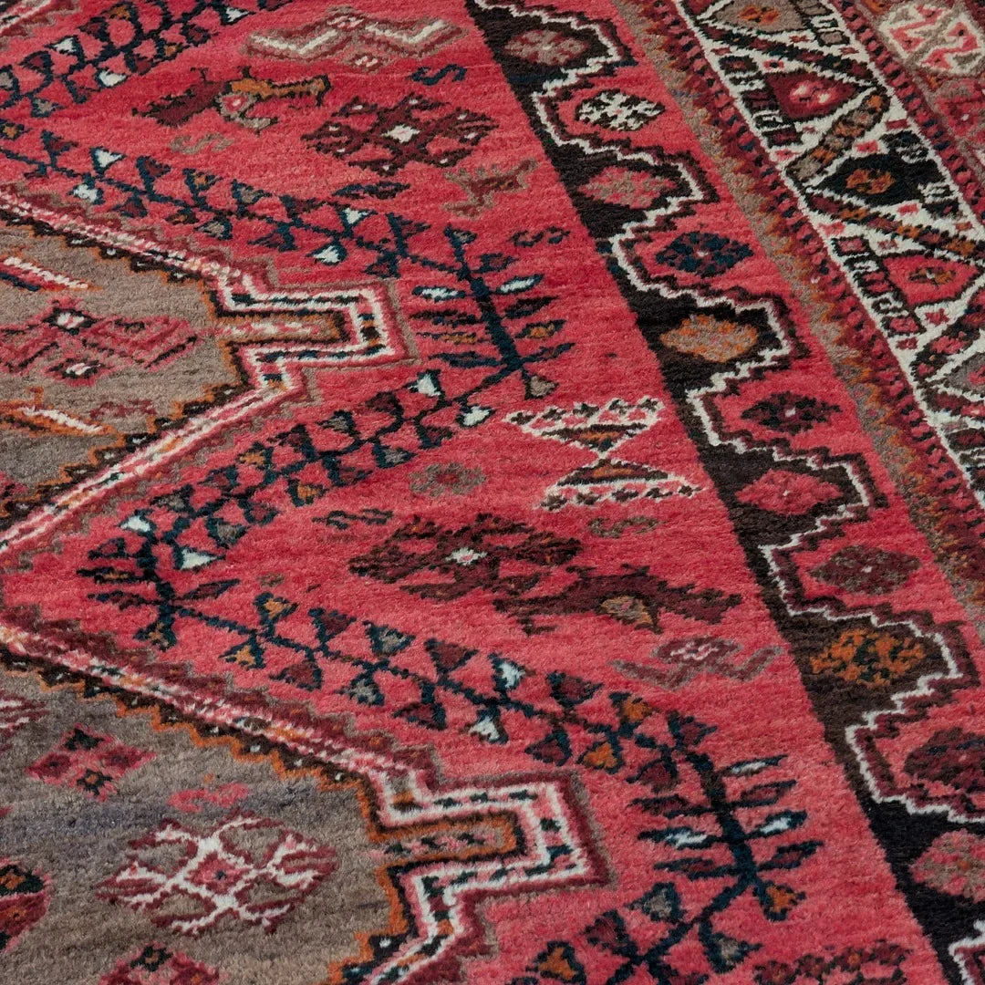 Pink and red patterned vintage rug with geometric tribal designs and bold borders