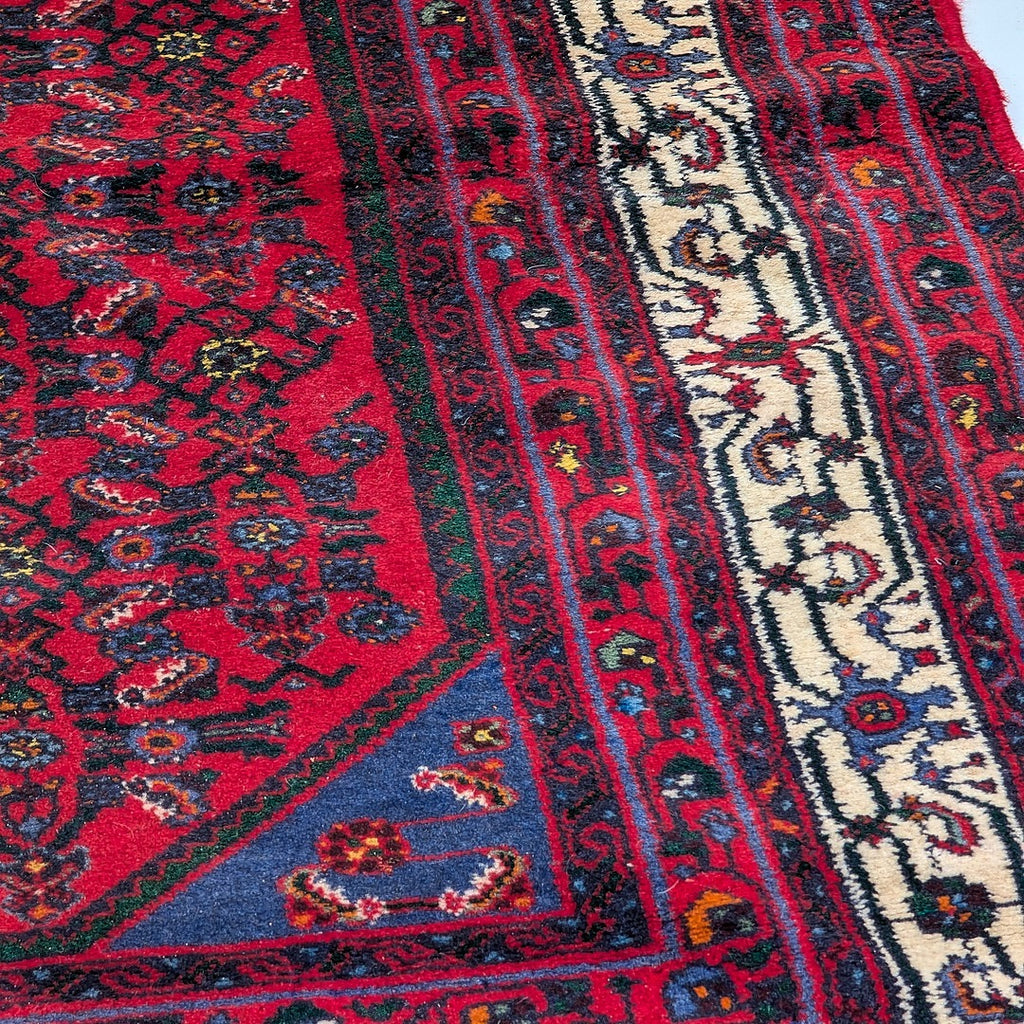 Close-up of vintage Persian-style rug with intricate red, blue, and cream geometric patterns and floral motifs