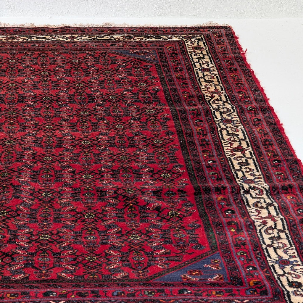 Detailed corner of red vintage Persian-style rug with intricate geometric patterns and cream border