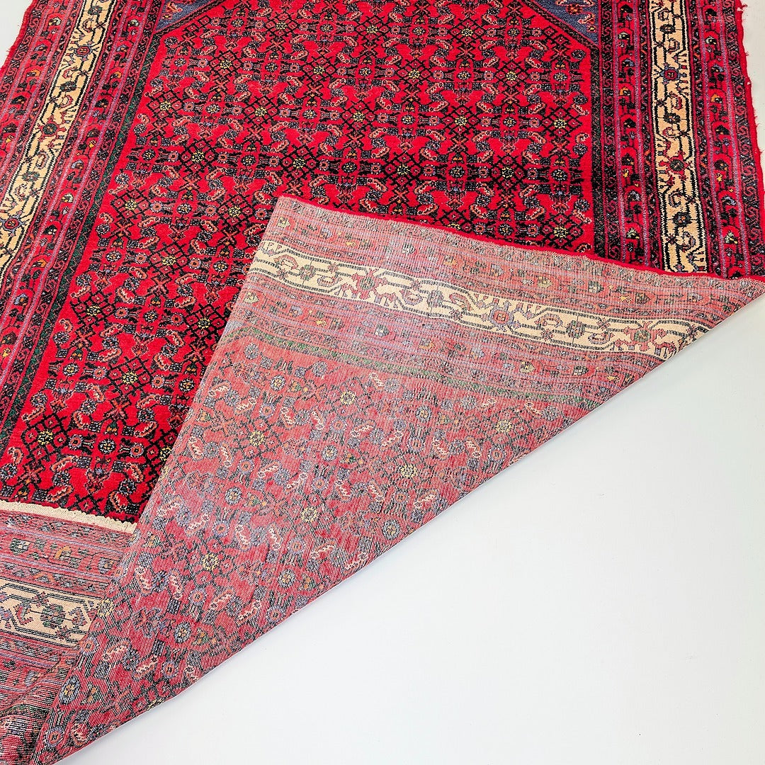 Red vintage Persian-style kilim rug with intricate geometric and floral patterns, folded corner showing backside