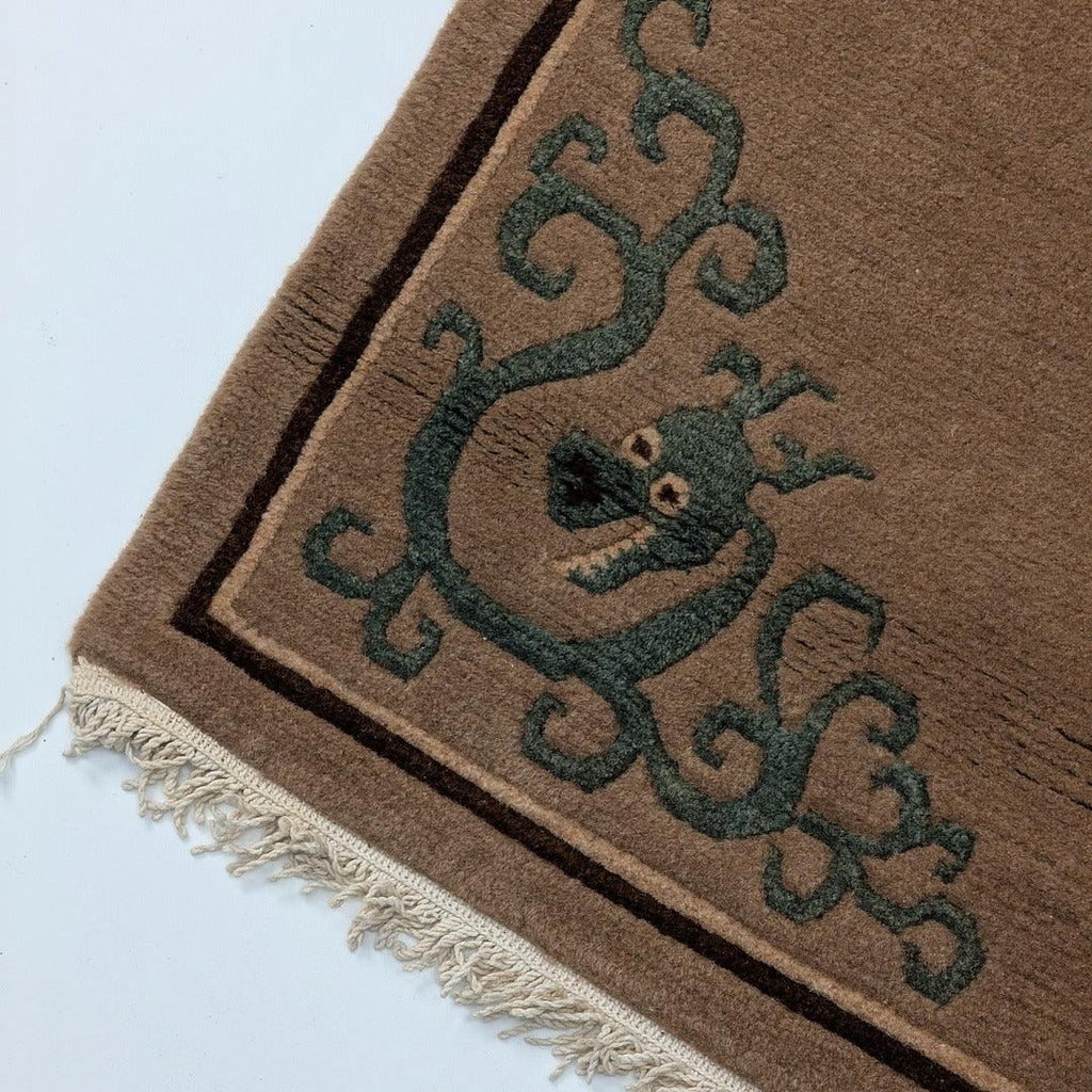 Corner of brown wool rug with green dragon pattern and fringed edge