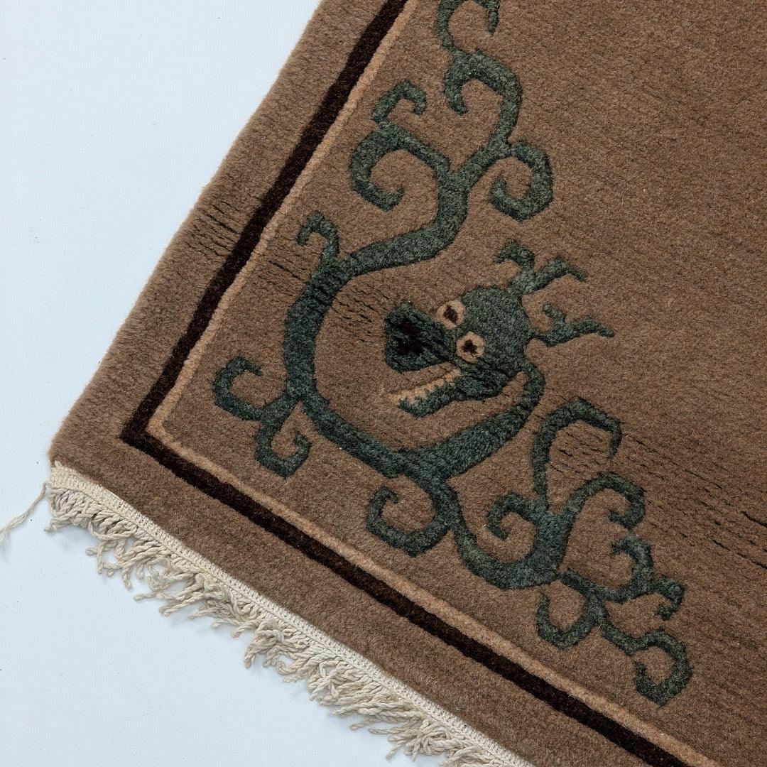 Corner of brown wool rug with green dragon pattern and fringed edge