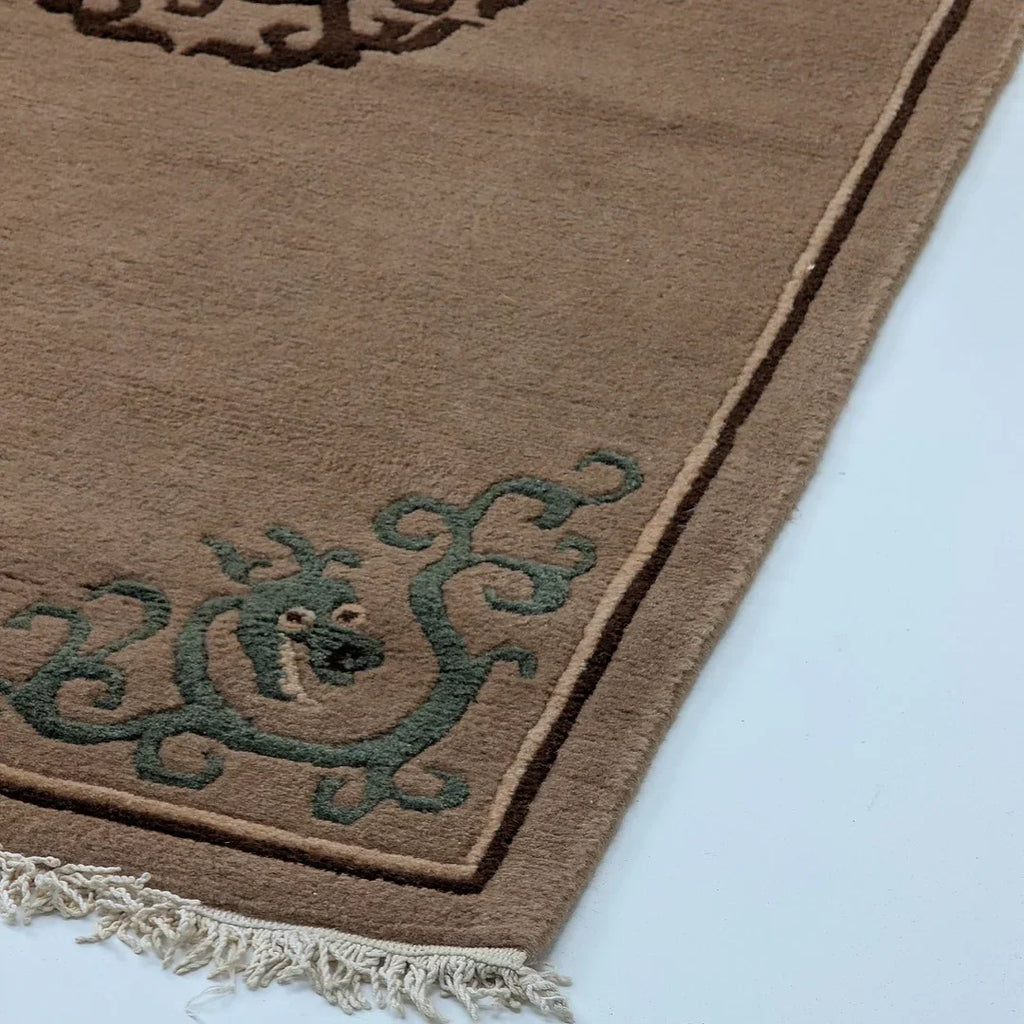 Brown wool rug with green dragon motif and fringe on white surface