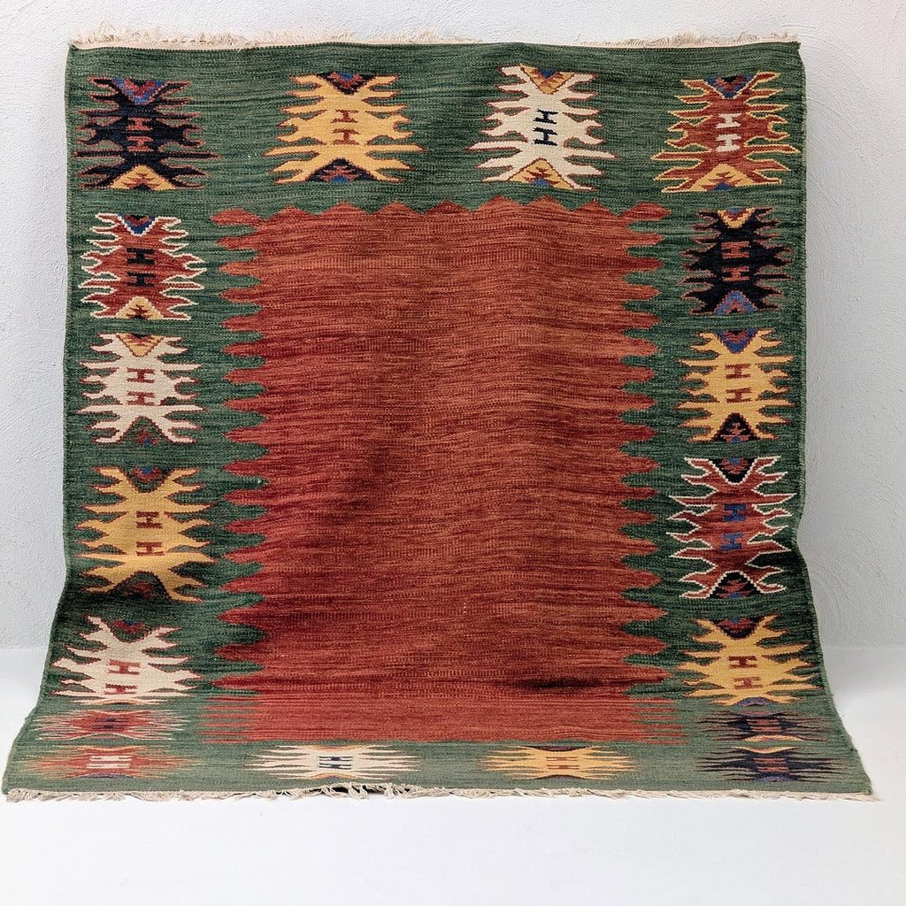 Handwoven rug with red center, green border, and geometric tribal patterns
