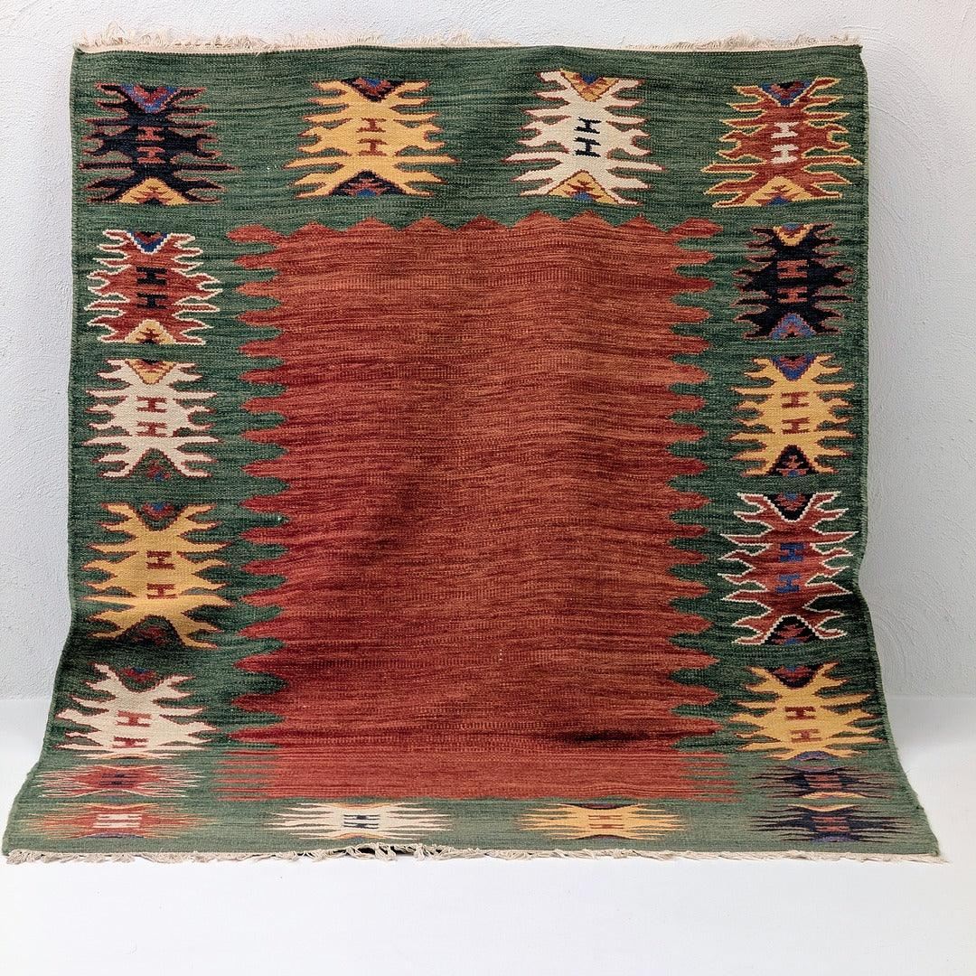 Handwoven rug with red center, green border, and geometric tribal patterns