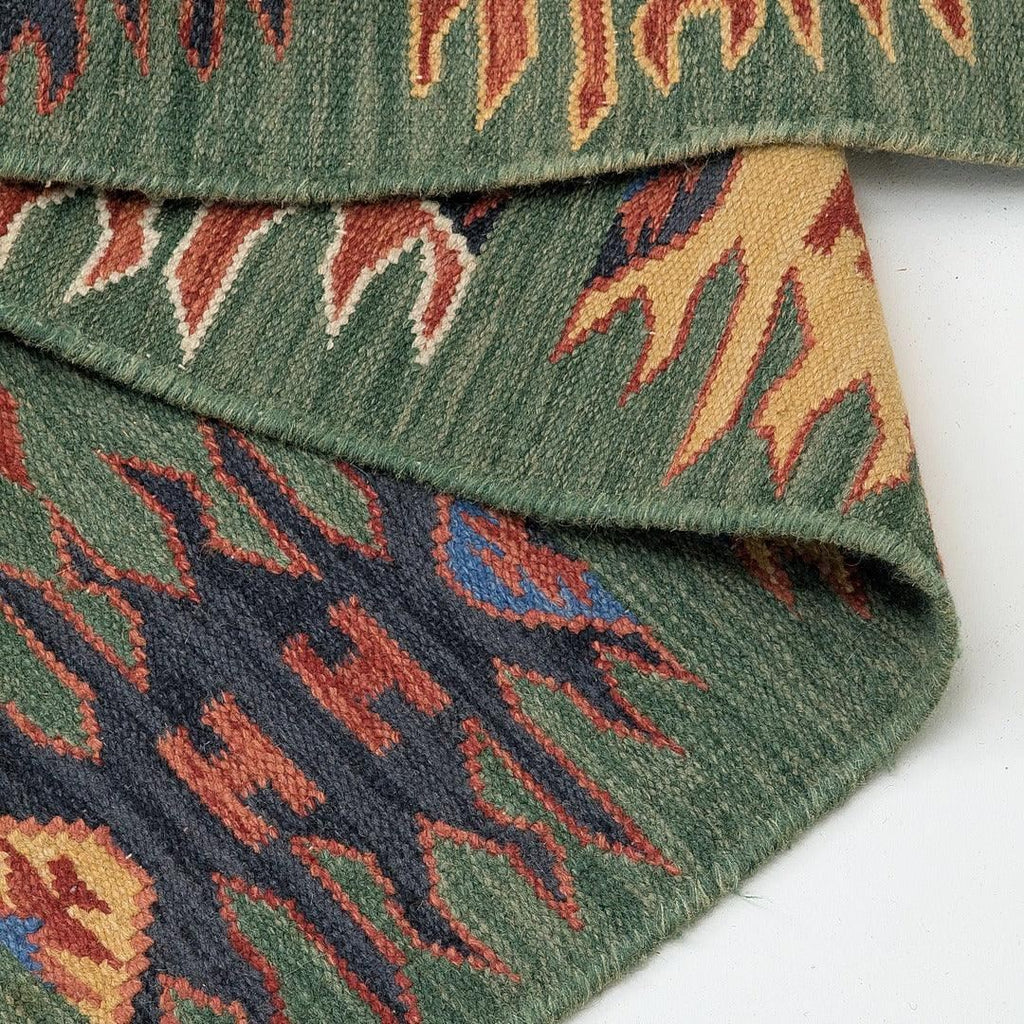 Green handwoven kilim rug with geometric tribal pattern, folded on white background