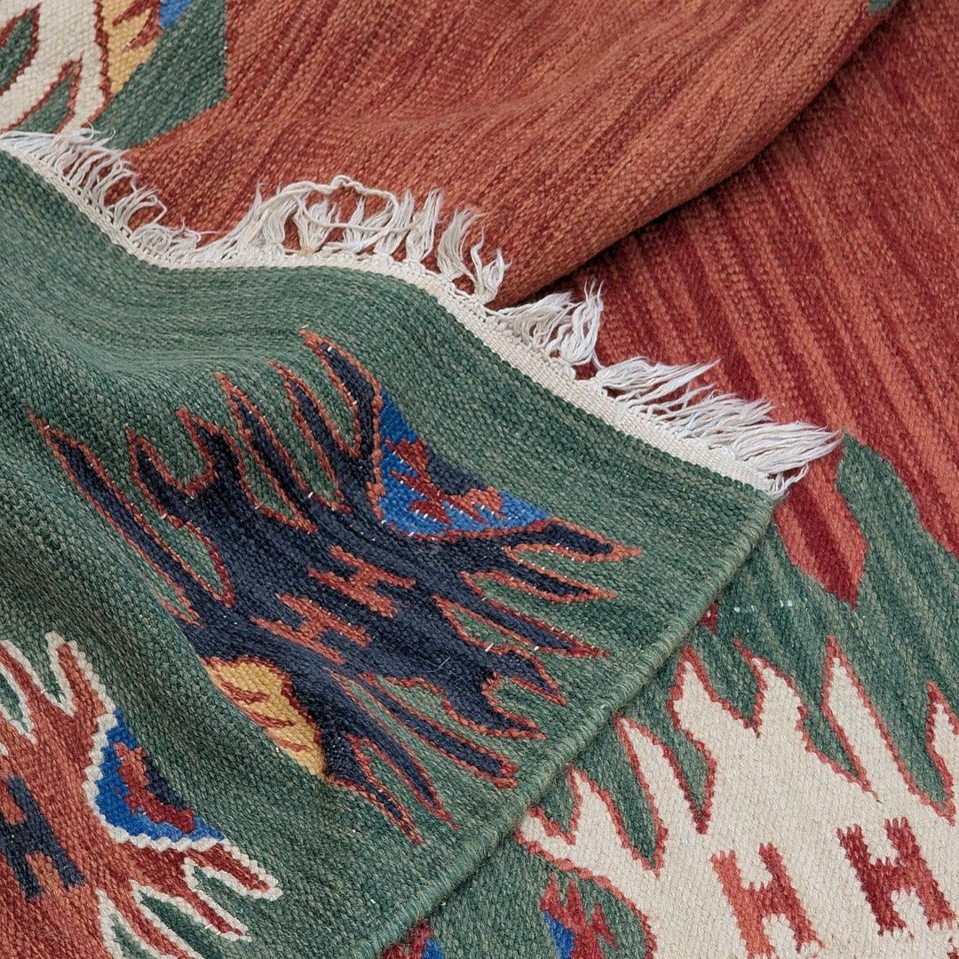 Handwoven kilim rug with geometric tribal patterns in earthy red, green, and beige colors